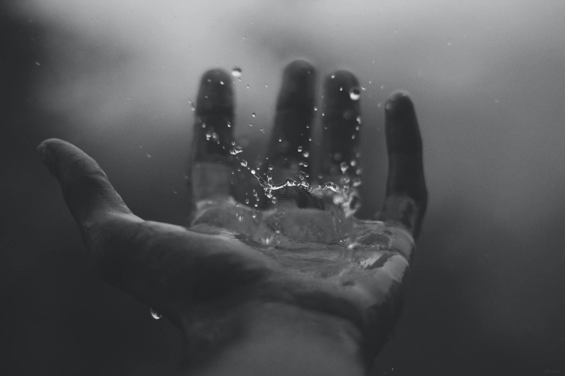 czarno białe zdjęcie przedstawiające ludzką dłoń, na którą pada deszcz
