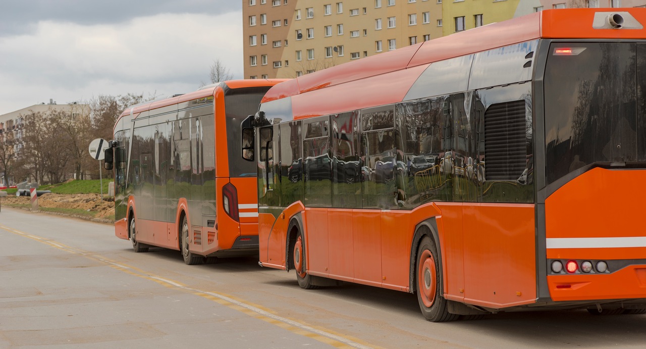 pomarańczowe autobusy miejskie obok dużego bloku